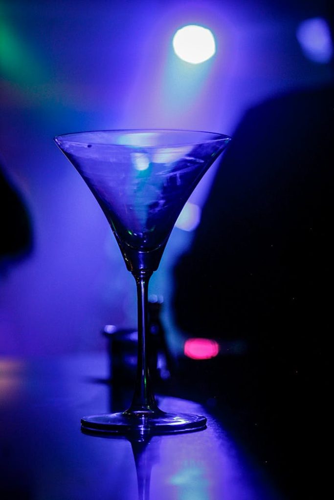 A crystal martini glass glows under vibrant nightclub lighting.