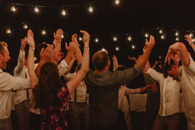 Guests dancing with hands in the air under string lights